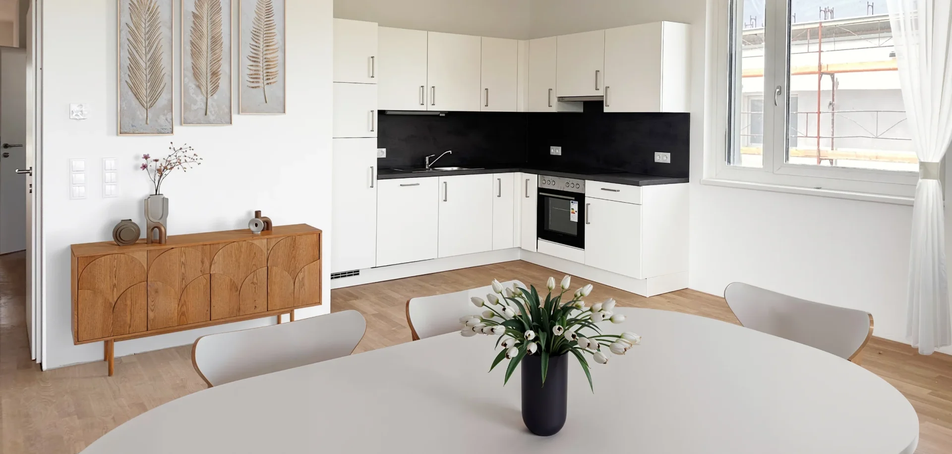 TRI_WohnungFinden_01 Moderne Wohnküche mit Esstisch, weißen Fronten und stilvollem Dekor in heller Umgebung.